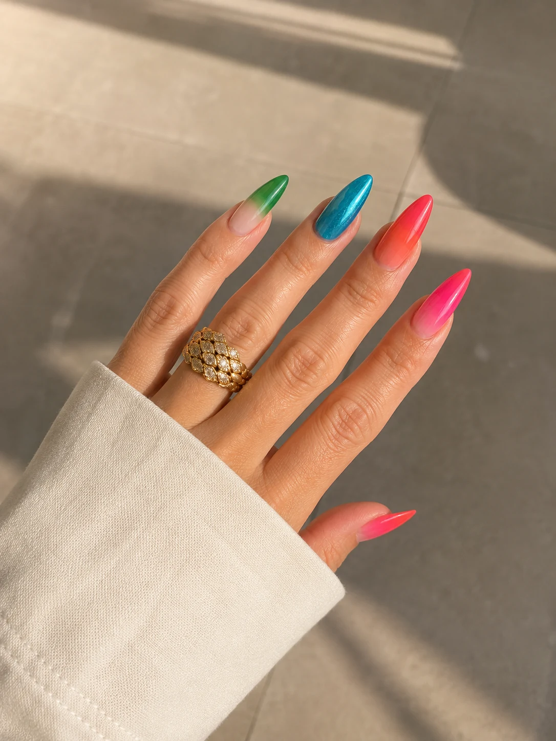 Main aux ongles stiletto verts, turquoise, corail et roses sous la lumière, création d’Anabelle